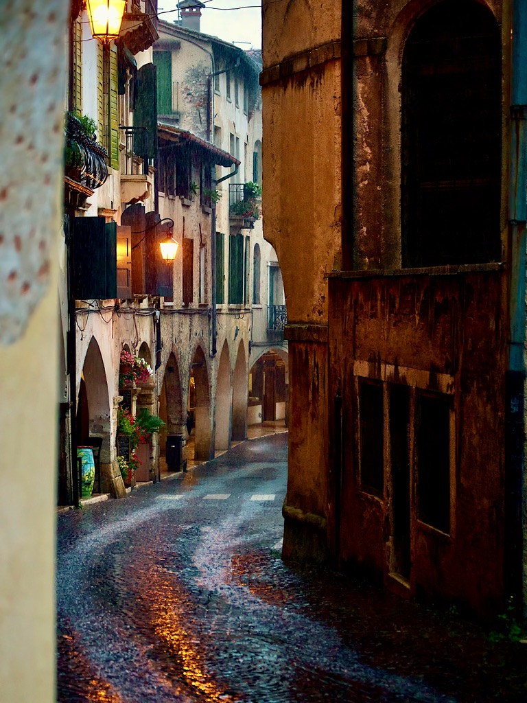 Rain-darkened lane beneath an arcade in Asolo